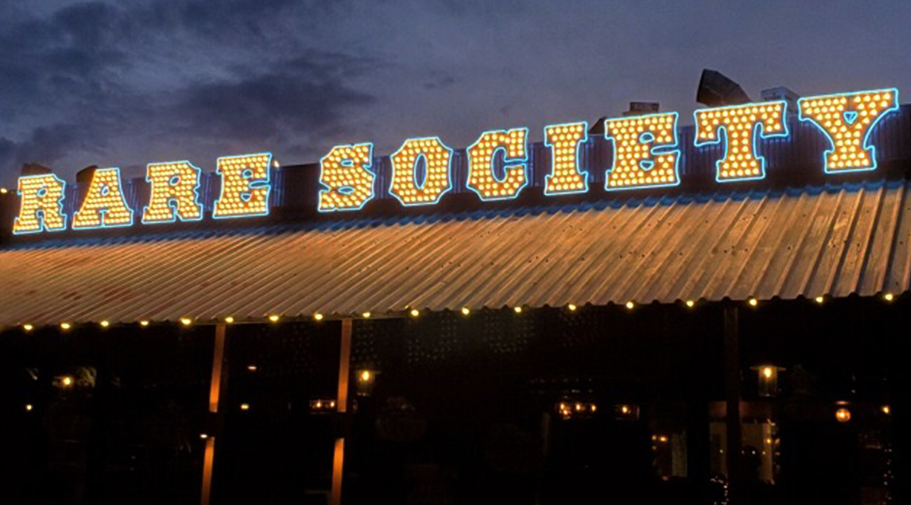 Exterior of restaurant at night with Rare Society sign spelled out in vegas-style lettering