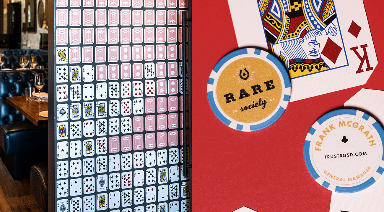 Dipdick of Rare Society custom playing card wall installation next to Rare Society blue and gold poker chip business "cards" against a king playing card and red background